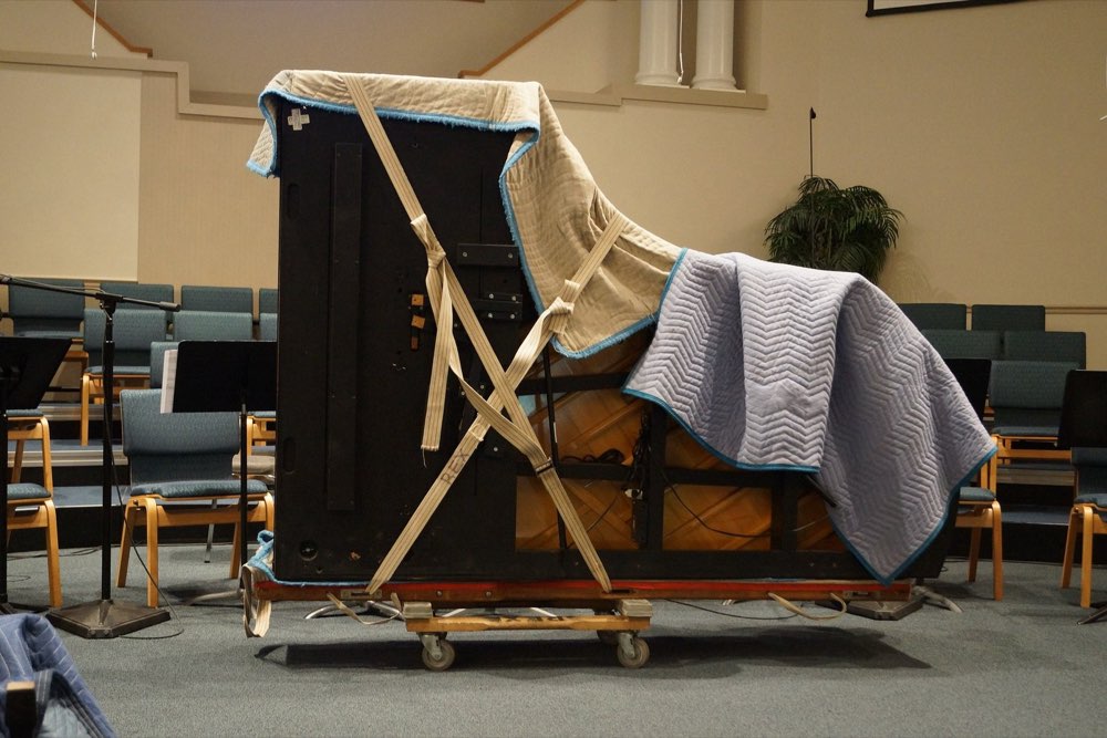 Upright piano wrapped in moving blankets and strapped to a dolly